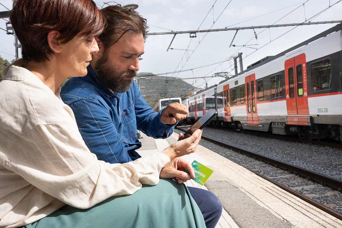 Dos personas consultan el móvil con su T-mobilitat.